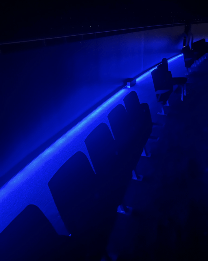 A dimly lit cinema seating area featuring blue ambient lighting along the walls and seats.