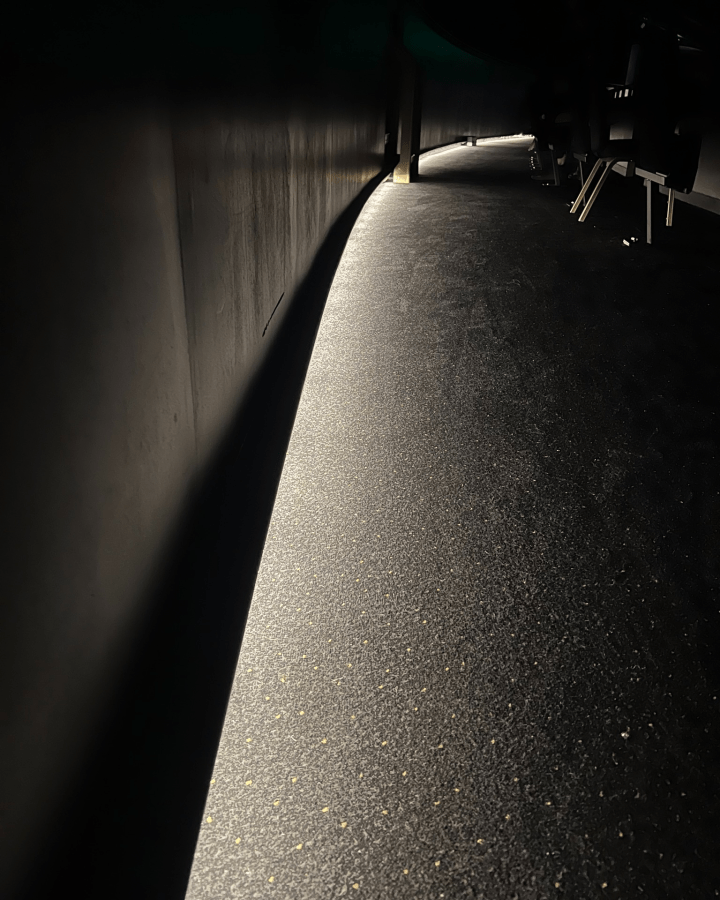 A dimly lit corridor with a glowing light along the floor, showcasing a textured dark surface.